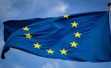En blå EU-flagga med tolv gula stjärnor vajande mot en blå himmel.